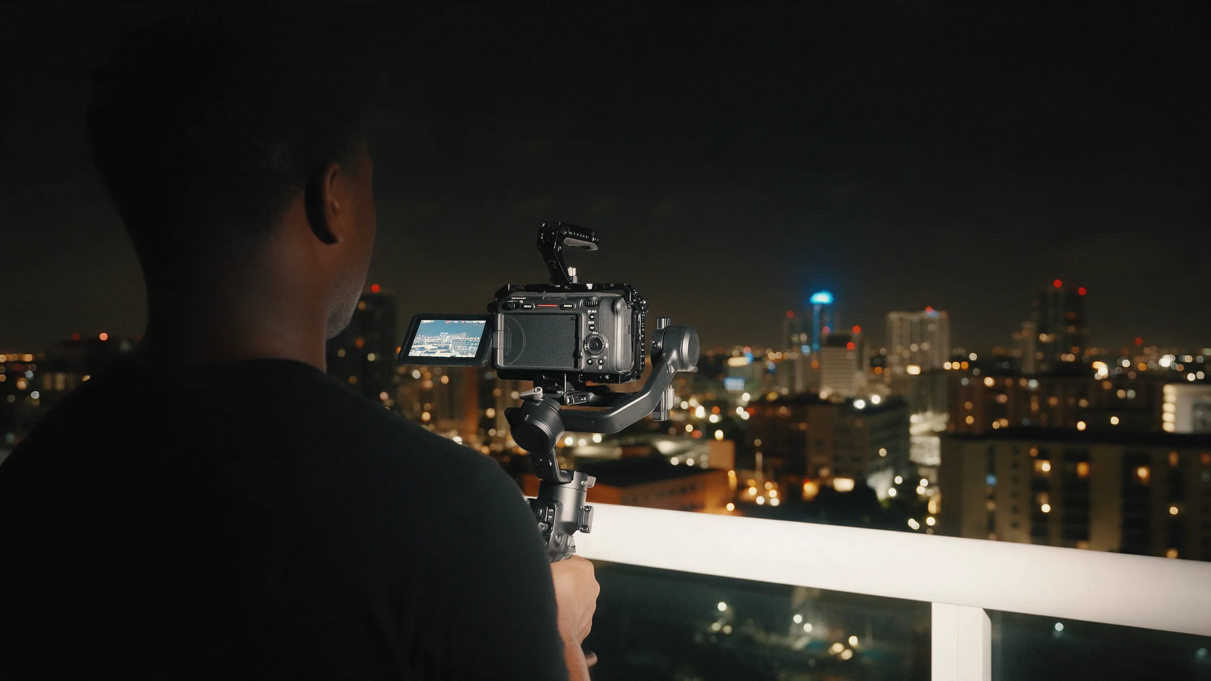 A videographer on a Fort Lauderdale rooftop at night, working a rigged cinema camera against the lit skyline