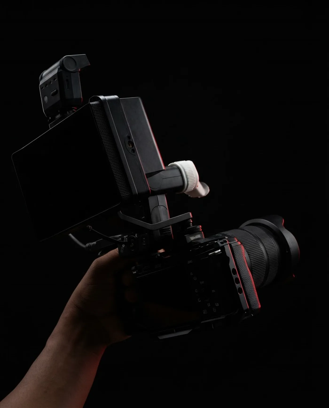 A cinema-rigged mirrorless camera with a field monitor and flash, lit against black