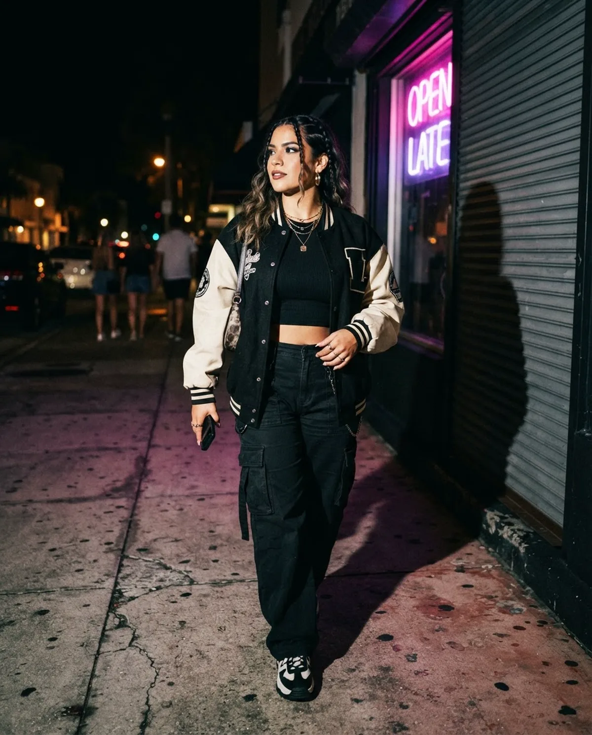 A creator in a varsity jacket mid-stride on a sidewalk at night, lit by flash against a neon sign