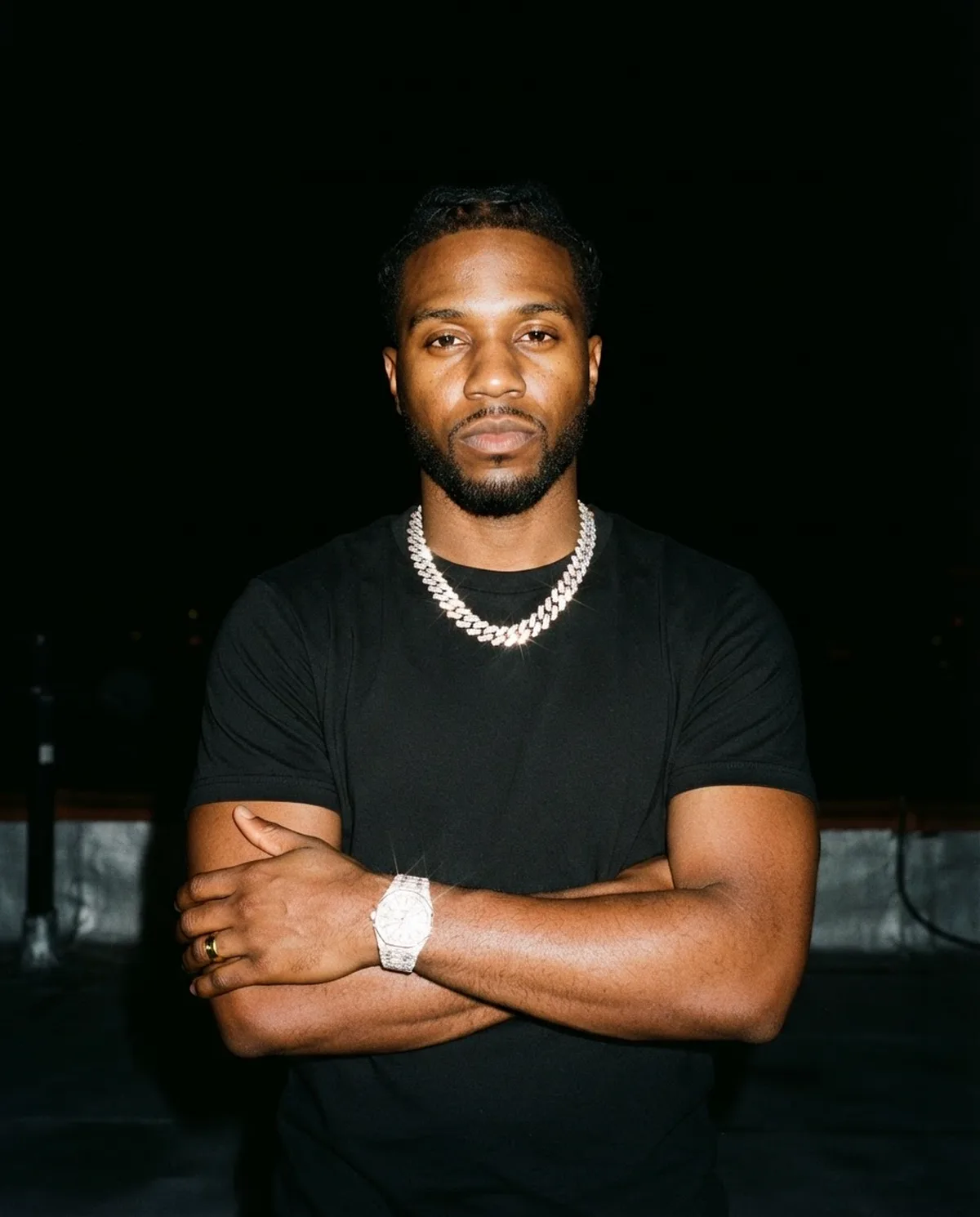 A recording artist in a black tee and chain photographed with flash against a black background
