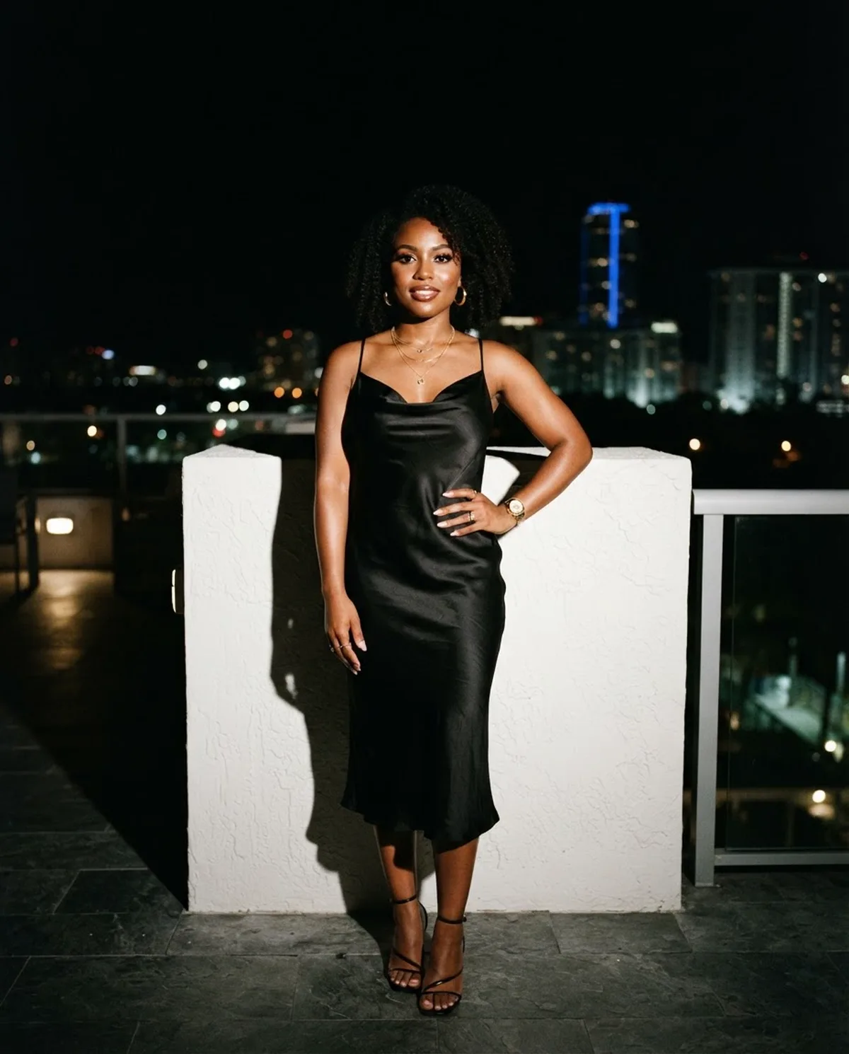 A creator photographed with flash on a rooftop terrace, the city lights behind her